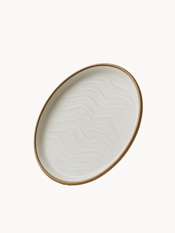 Ceramiczny talerz o matowym wykończeniu w odcieniu złamanej bieli, ozdobiony strukturalnym wzorem przypominającym wydmy piaskowe i wykończony naturalnym brązowym rantem.