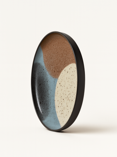 Duży ceramiczny talerz z czarnym rantem oraz  abstrakcyjnym wzorem z w odcieniach brązu, beżu, jasnego błękitu i czerni. Talerz jest zaprezentowany w pozycji pionowej pod lekkim kątem na jednolitym białym tle.