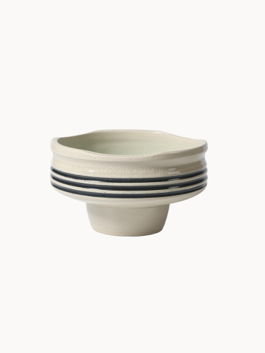 Ceramiczna miska na podwyższeniu w jasnokremowym kolorze, pokryta spękanym szkliwem z trzema czarnymi paskami wokół środka.